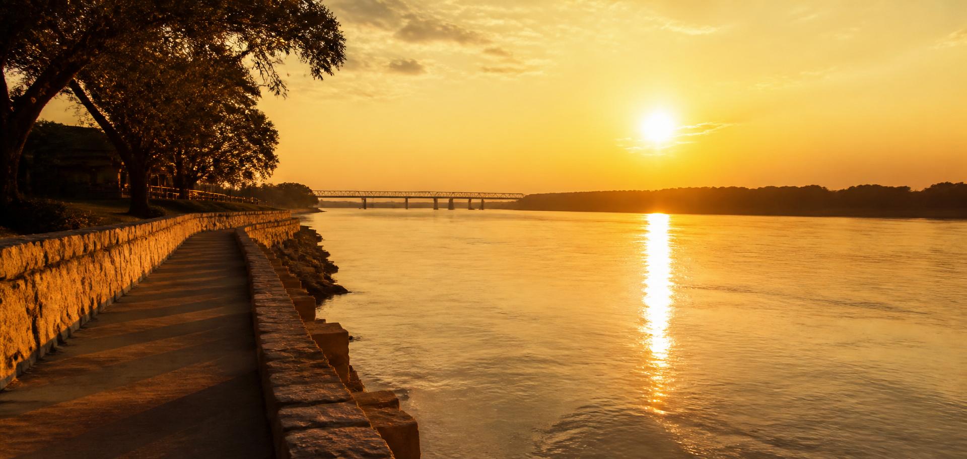 Golden-hour sunset over the Mississippi River seen from a limestone riverfront walkway